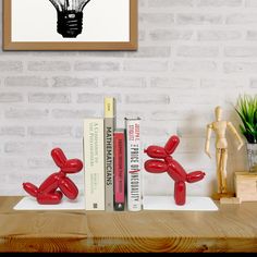 two red balloon dogs sitting on top of a table next to books and a plant