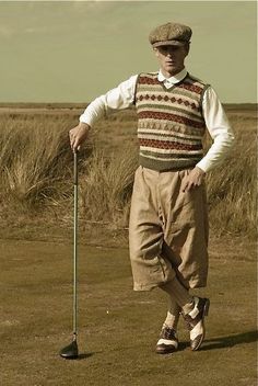 a man standing on top of a grass covered field holding a golf ball and club