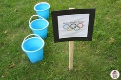 four blue buckets sitting next to a sign with the olympic rings on it in grass