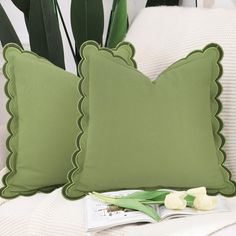 two green pillows with scalloped edges sit on a white couch next to a potted plant