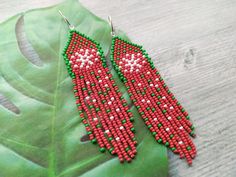 a pair of red and green beaded earrings sitting on top of a leaf