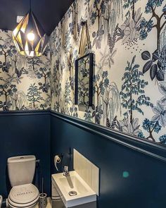 a toilet and sink in a room with wall paper on the walls, along with a light fixture