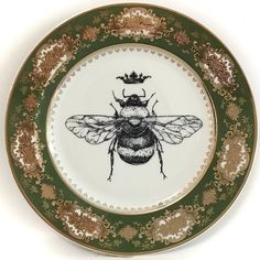 a plate with a drawing of a bee on it's side and gold trimming around the edge