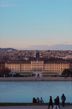 people sitting on the edge of a body of water in front of a large building