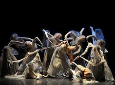 a group of dancers with their arms in the air and one person holding a stick