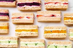 several sandwiches are arranged in rows on a white surface, each with different colored fillings