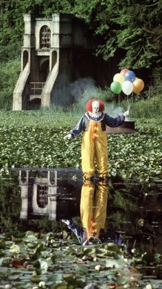 a clown is standing in the water with balloons