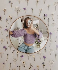 a woman taking a selfie in front of a mirror with flowers on the wall