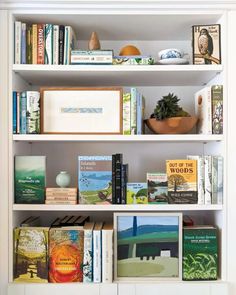 a white book shelf filled with books next to a potted plant on top of a wooden table