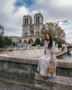 a woman sitting on the edge of a wall next to a body of water with a cathedral in the background