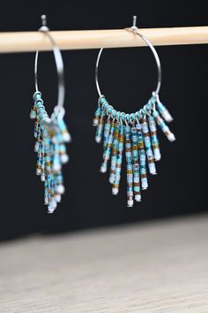 the hoop earrings are made out of glass beads and beaded with silver wire, which is hanging from a wooden bar