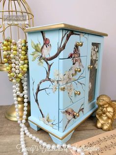 a blue cabinet with birds painted on it and pearls hanging from the top, next to a birdcage