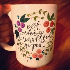 a person holding a coffee mug with the words eat sleep rest and repeat on it