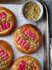 four pastries on a baking sheet with different toppings and seasoning in bowls