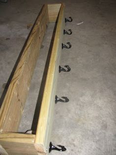 a wooden bench sitting on top of a floor next to some black hooks and screws