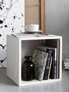 a book shelf with books and a coffee cup on it, in front of a black and white painting