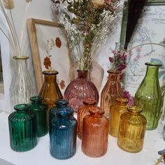 there are many different colored vases on the shelf together, including one with flowers in it