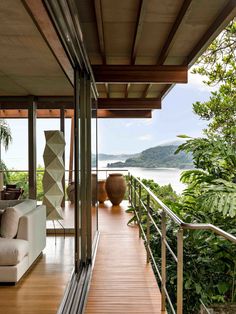 a living room filled with furniture next to a large window covered in greenery and overlooking the ocean