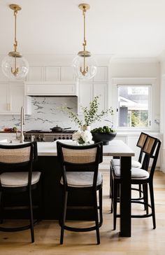 a kitchen with white cabinets, black chairs and a marble island in the center surrounded by wood flooring