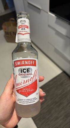 a person holding up a bottle of ice water in their hand, with the label smirnoff on it