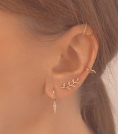 a close up view of a woman's ear wearing gold earrings with leaves on them