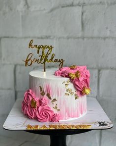 a pink and gold birthday cake with flowers on the top is sitting on a table