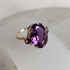 The ring is made from 14K solid yellow gold.Gemstone used is absolutely natural and ethically sourced. Details of the ring Gem: Purple Amethyst (1pcs) Gem size & shape: 17x12 mm & oval Center Gem weight: 9.30 carat Gem : Pink Tourmaline (2pcs) Gem size & shape : 4 mm round (2 pcs) Gem weight : 0.53 CTS Gem : Diamond (4pcs) Gem size & shape : 1.50 mm round (4 pcs) Gem weight : 0.060 CTS Total Stones weight : 9.89 CTS Gold purity: 14K (58.33% approx.) Gold weight: 2.69 grams  total weight of ring: 4.67 grams Fine emerald cut Purple Amethyst oval shape gemstone with pink tourmaline and diamond set on solid 14K yellow gold with its utmost precision.  The Gold purity is guaranteed and it comes with authentic 14 kt gold hallmark. CUSTOMISATION Since these Rings are handmade they are Nickel/Lead Luxury Amethyst Ring With Oval Cabochon, Luxury Antique Amethyst Ring, Luxury Handmade Gold Amethyst Ring, Purple Ruby Ring For Formal Occasions, Purple Oval Ruby Ring, Fine Jewelry, Elegant Purple Ruby Ring With Accent Stones, Formal Purple Sapphire Ring With Gemstone Accents, 14k Gold Purple Amethyst Ring, Elegant Purple Ruby Ring