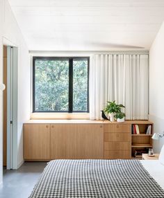 a bed sitting under a window next to a wooden shelf filled with books and plants