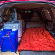 the back end of a van filled with luggage and water bottles next to a sleeping bag