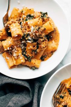 two plates of pasta with meat, cheese and spinach on them next to a fork