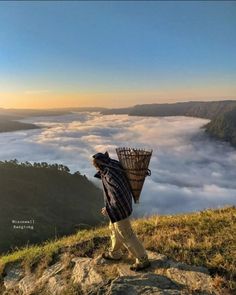 a person carrying a basket on top of a hill above the clouds in the sky