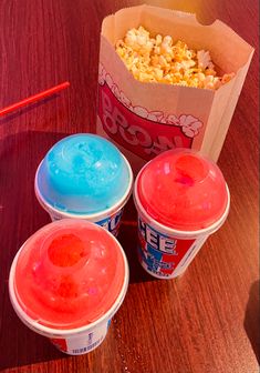 three buckets of ice cream next to a cup of popcorn on a wooden table