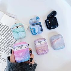 a person holding an airpods case in front of several other cases on top of a table