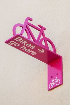 a pink bike sign mounted to the side of a wall next to a white wall