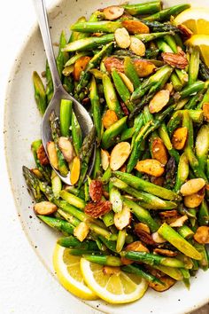 a white bowl filled with asparagus, almonds and lemon wedges on top of a table