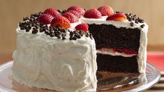 a chocolate cake with white frosting and strawberries on top is sitting on a plate