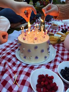 two people lighting candles on a cake with berries and strawberries in front of them