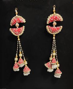 two red and white earrings with pearls hanging from it's sides on a black surface