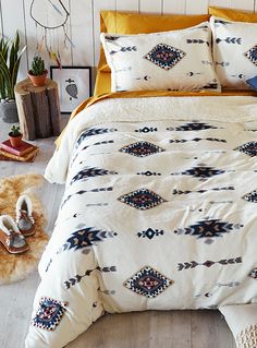 a bed with white and yellow comforters in a bedroom next to potted plants