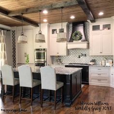 a large kitchen with white cabinets and black island in the center is decorated with hanging lights