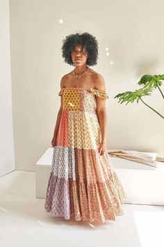 a woman standing in front of a white wall wearing an off the shoulder dress with multicolored patterns