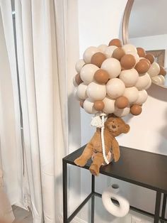 a teddy bear sitting on top of a table with balloons in the shape of animals