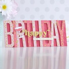 a pink birthday card with the words happy on it and a wine glass in front