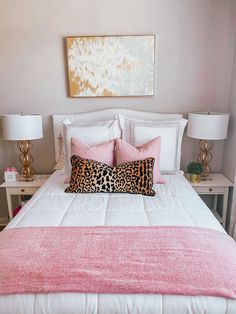 a white bed topped with pink pillows and a leopard print throw pillow on top of it