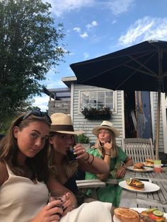 two women sitting at an outdoor table with food and drinks in front of the house