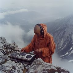 a man in an orange jacket and headphones is playing music on top of a mountain