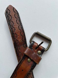 a brown leather belt with a metal buckle on the bottom and an intricate design on the side