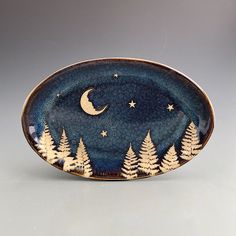 a blue plate with white trees and the moon in the night sky on grey background