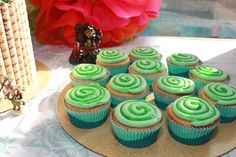 cupcakes with green frosting sitting on a gold plate next to a vase