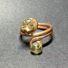 two gold rings with green glass stones on each one, sitting on a gray surface